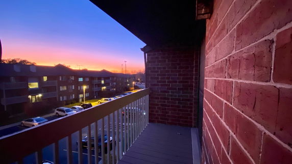 View from a balcony showing sunset sky and distant residential buildings.