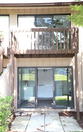 Front view of a two-story house with a wooden balcony on the upper level and sliding glass doors on the lower level.