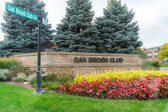 Front view of a building with a stone wall sign reading 'Oak Brook Club'.