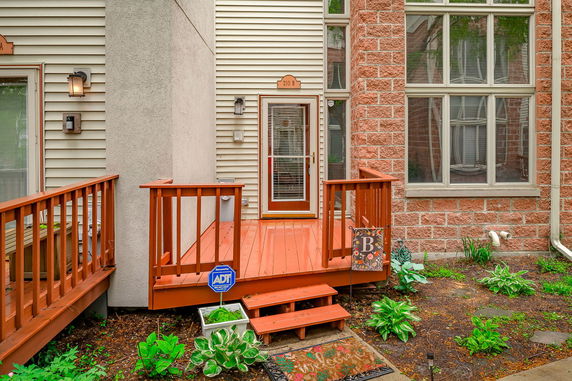 Front view of a house entrance with a small wooden deck and stairs, featuring a door with a glass panel and large windows to the side.