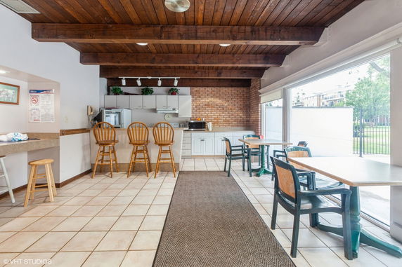 Interior view of a clubhouse with a kitchen area, bar stools, and tables with chairs.