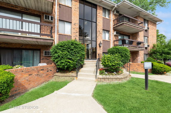 Front view of a multi-story brick apartment building with balconies and a central entrance.