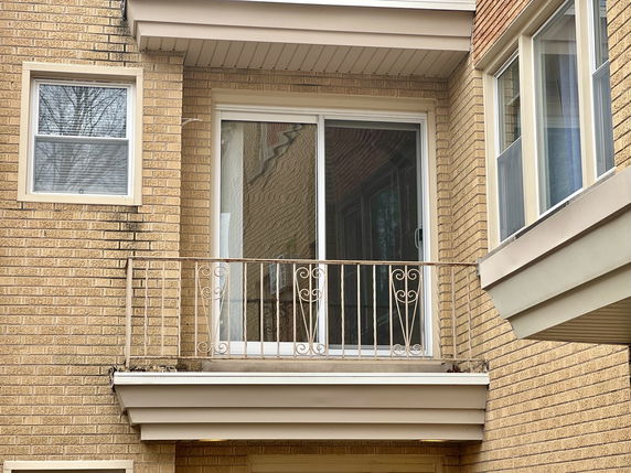 Front view of a brick house with a small balcony and sliding glass door.