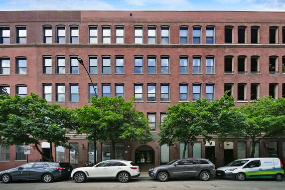 Front view of a multi-story brick building with numerous windows and parked cars in front.