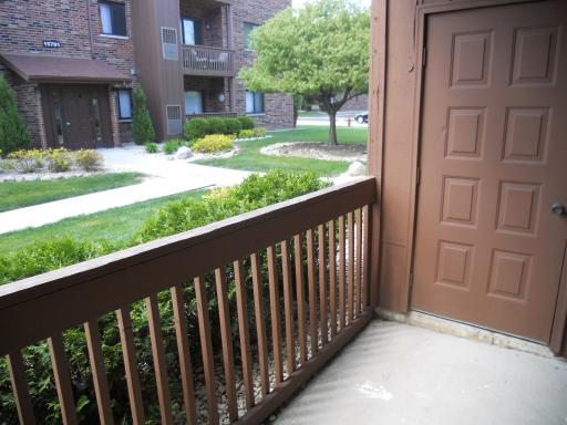 View from a porch looking out at a pathway, with a tree and brick apartment building in the background.