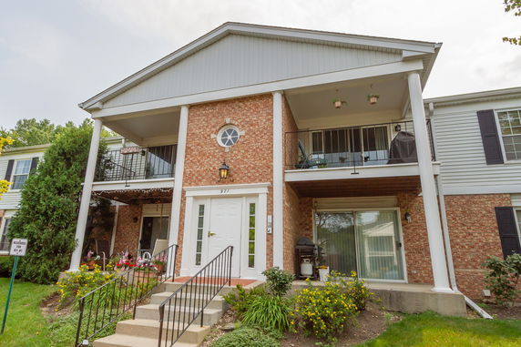 Front view of a two-story house with brick and siding exterior, featuring a covered balcony and entrance.