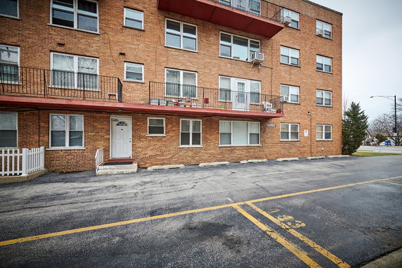 Front view of a multi-story brick building with balconies and parking space.