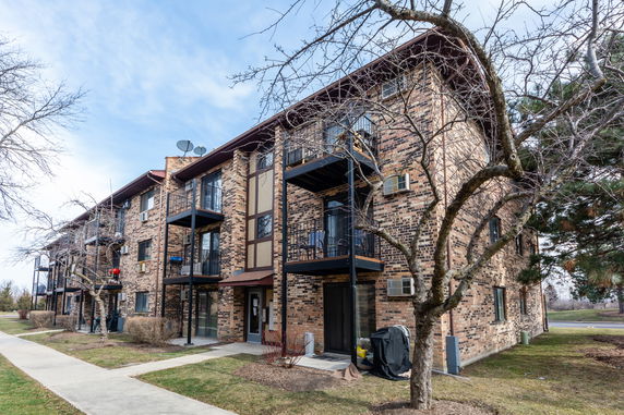 Front view of a multi-story brick apartment building with balconies and air conditioning units.