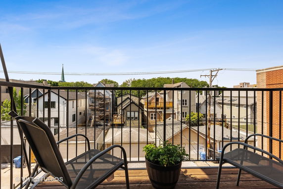 View from a balcony with chairs and potted plants overlooking residential buildings.