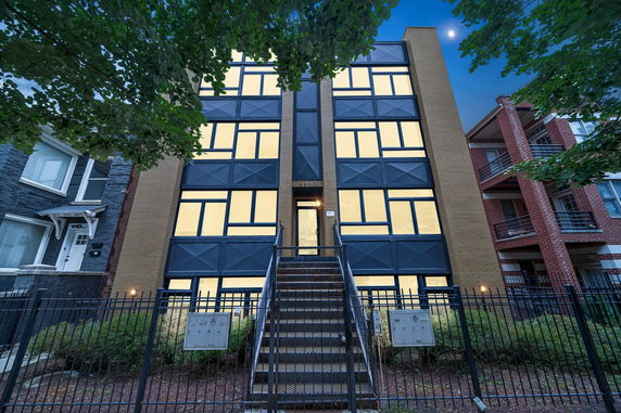 Front view of a modern multi-story apartment building with a staircase leading to the entrance.