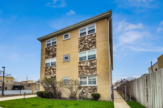 Side view of a three-story apartment building with beige brick and stone facade.