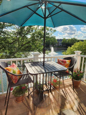 Patio area with umbrella overlooking a lake and fountain.