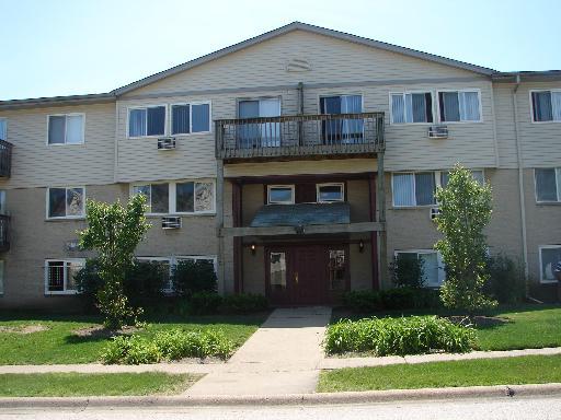 Front view of a three-story residential building with multiple balconies and air conditioning units.
