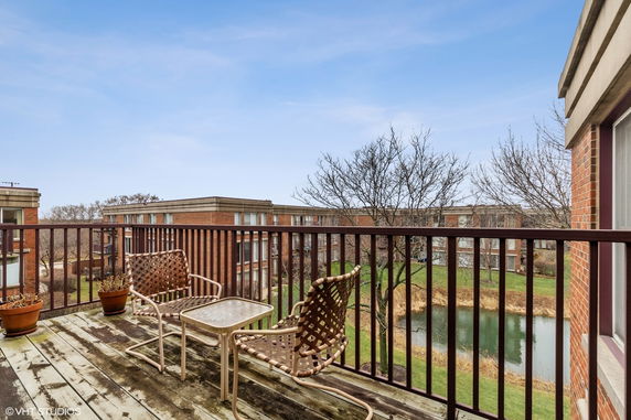 Rooftop balcony with chairs and table overlooking buildings and pond.