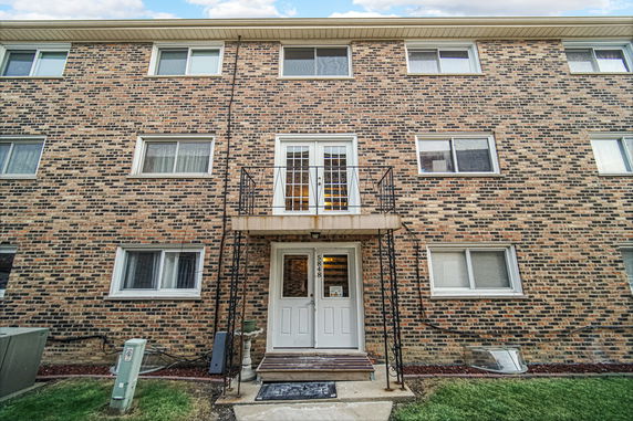 Front view of a three-story brick building with multiple windows and a balcony above the entrance door.