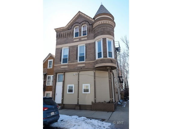 Front view of a three-story house with a turret and brick facade.