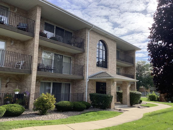 Front view of a three-story brick apartment building with balconies.