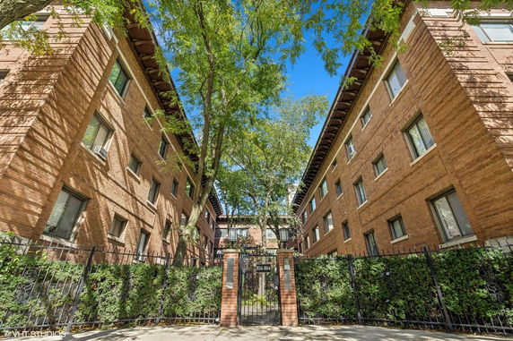 Front view of a multi-story brick apartment building with a central entrance gate.