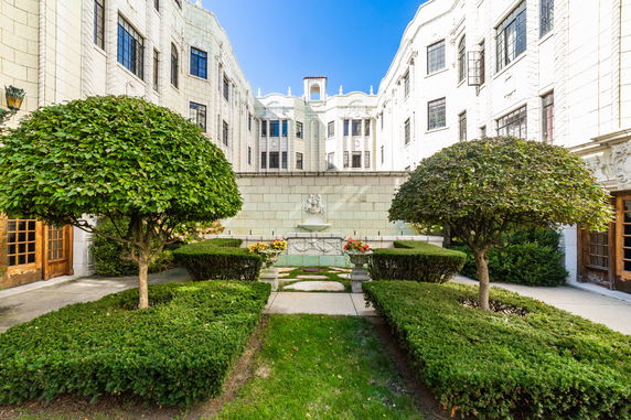 Front view of a multi-story building with a courtyard and symmetrical landscaping.