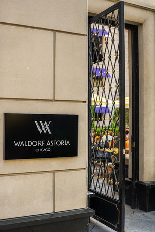 Front entrance of a building with an open iron-gated door and a sign reading 'Waldorf Astoria Chicago.'