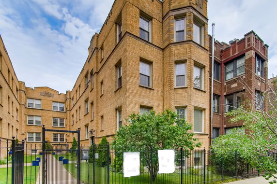 Front view of a multi-story brick apartment building with gated entrance.