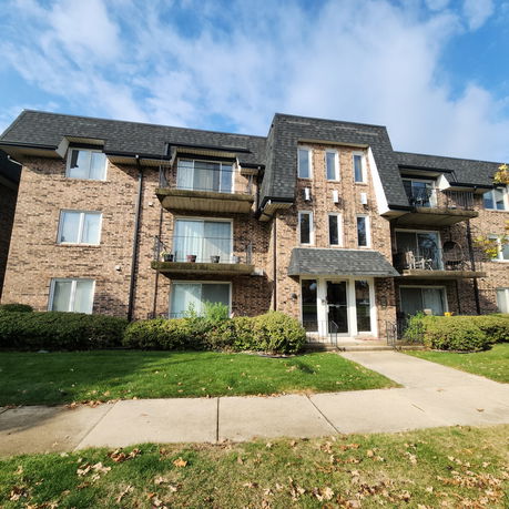 Front view of a multi-story brick apartment building with balconies.
