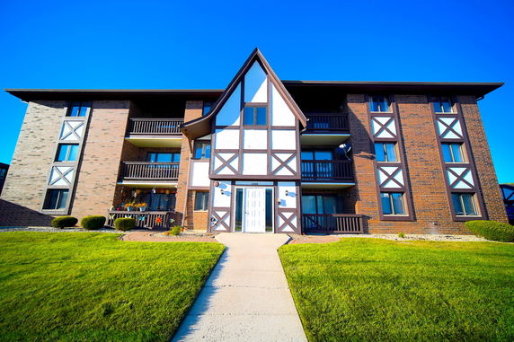 Front view of a multi-story apartment building with a central peaked roof and brick facade.
