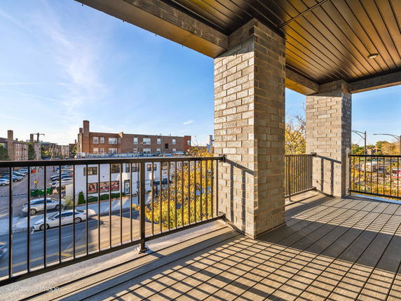 View from a covered outdoor balcony overlooking a street and buildings.