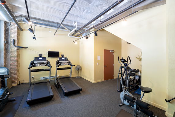 Indoor gym area equipped with treadmills, exercise bike, and weight racks.