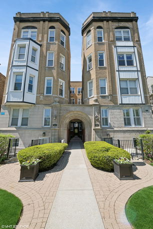 Front view of a multi-story residential building with an arched entrance and bay windows.