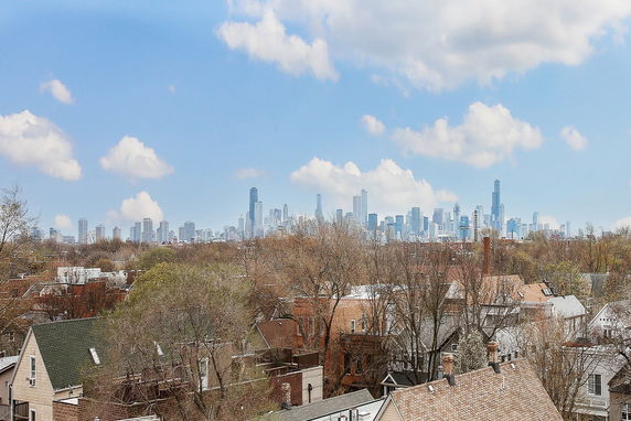 Panoramic view of a city skyline with trees and residential rooftops in the foreground.