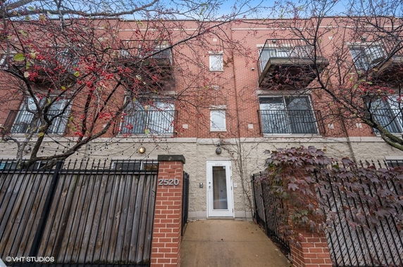 Front view of a multi-story brick building with balconies and a gated entrance.