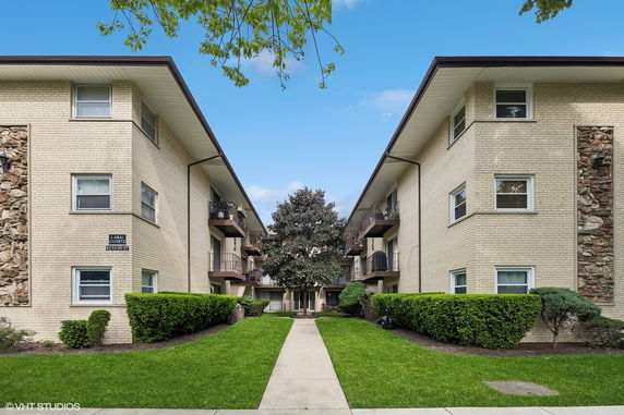 Front view of a multi-story apartment building with beige brick exterior and small balconies.