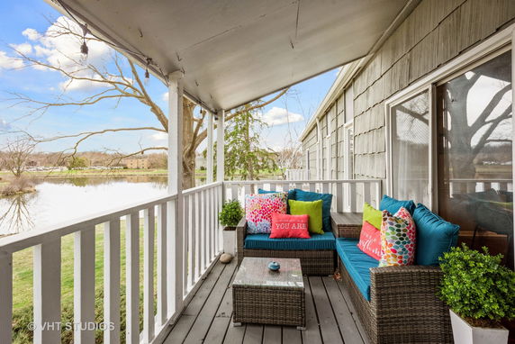 Covered outdoor patio with seating, overlooking a lake and trees.