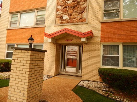 Front view of a multi-story brick building with a decorative stone section and a small overhang above the entrance.
