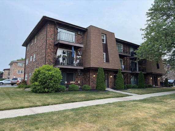 Front view of a three-story brick apartment building with balconies.