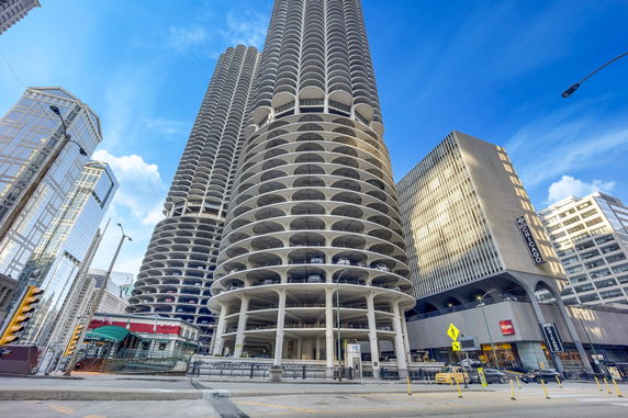 Front view of two cylindrical skyscrapers with multiple balconies and a modern glass building beside them.