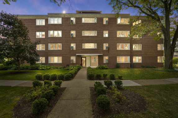 Front view of a multi-story brick building at dusk with illuminated windows.