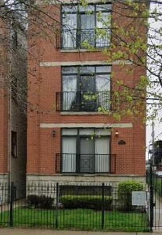 Front view of a multi-story brick building with a fenced front yard.