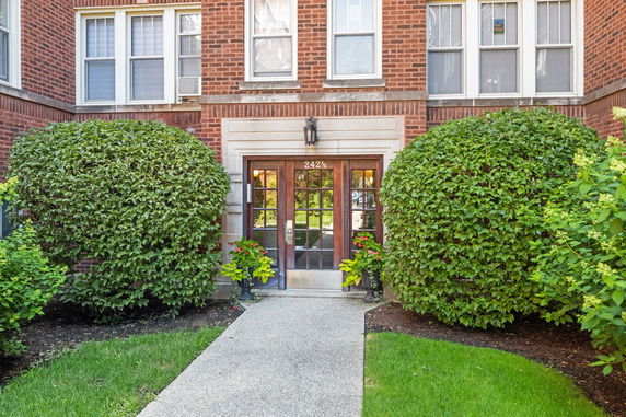 Front view of a brick building entrance with a glass door and surrounding shrubbery.