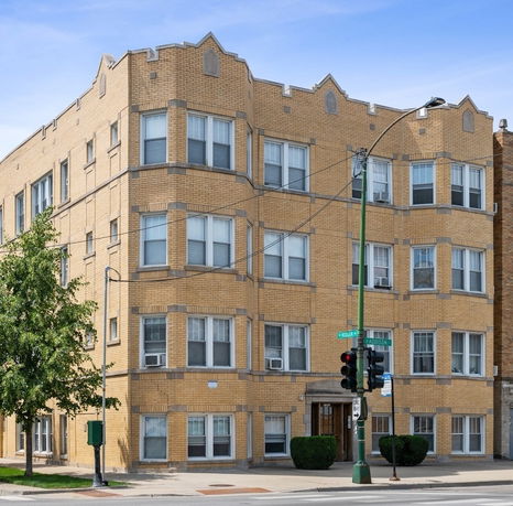 Front view of a multi-story brick apartment building at a street corner.