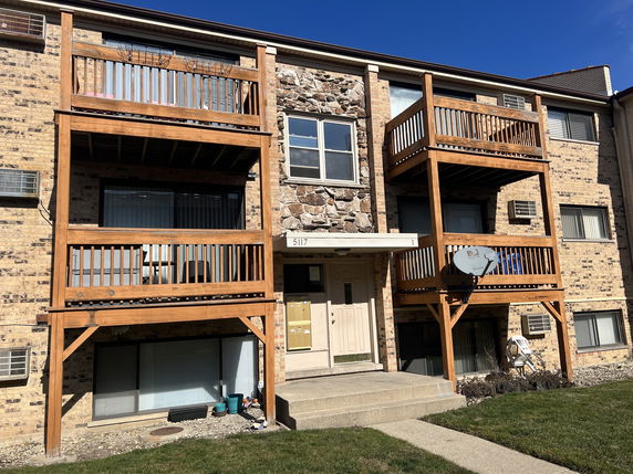 Front view of a multi-story apartment building with balconies and brick facade.