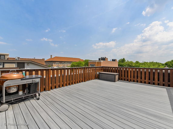 Rooftop deck with wooden railing and a grill.