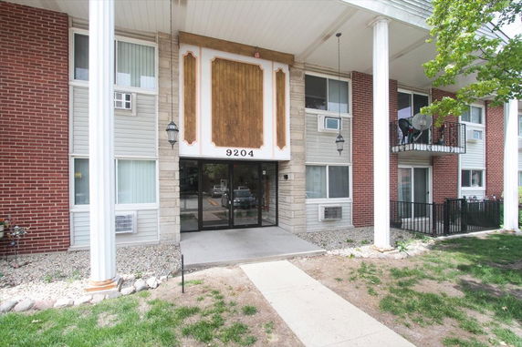 Front view of a multi-story brick and siding building with large pillars and a central entrance.