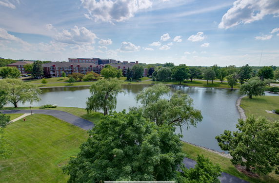 View of a lake surrounded by trees and a building in the background.