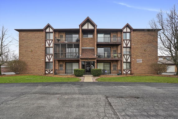 Front view of a three-story brick apartment building with balconies.