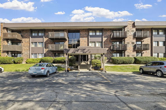 Front view of a multi-story apartment building with balconies and a parking area.