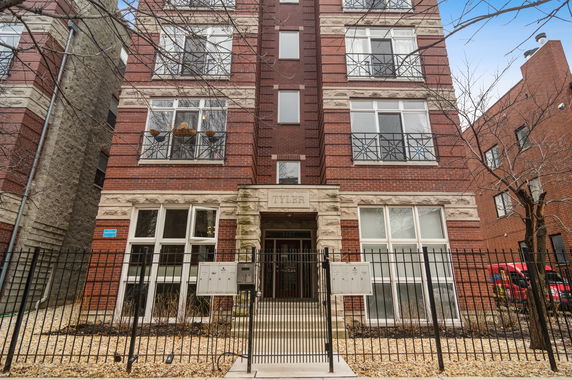 Front view of a multi-story brick building with large windows and a gated entrance.