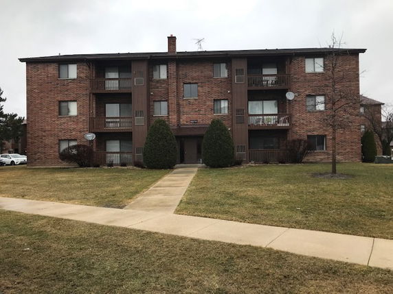Front view of a three-story brick apartment building with balconies.