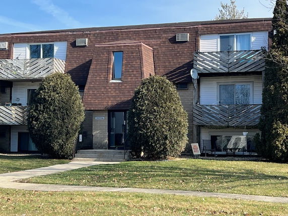 Front view of a two-story residential building with balconies and brown shingle roofing.
